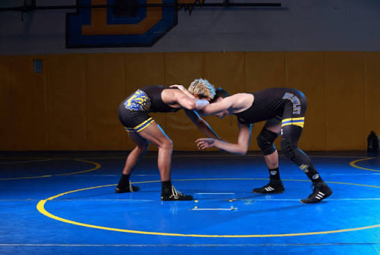 Two Brawley wrestlers squaring up on the blue mat in the wrestling room
