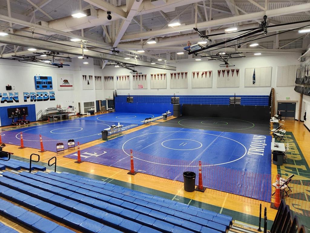 Three wrestling mats laid out in a gym before a tournament, bleachers empty
